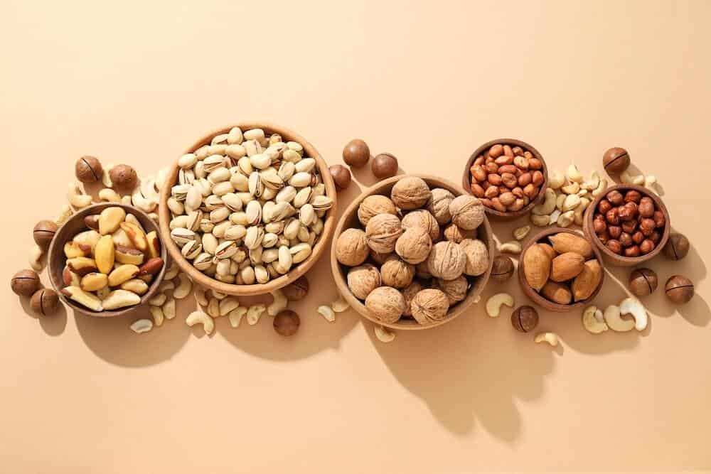 Foods That Help You Sleep Better: What to Eat for Deeper, Restful Nights - various nuts wooden bowls beige background 7 nuts and seeds